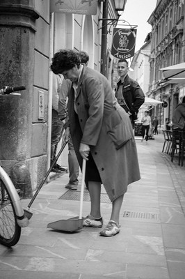 Foto på gammal kvinna som städar gata.